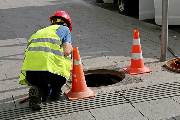Utility worker inspecting sewer system with cones—part of water utility solutions and monitoring systems in Texas Utility worker inspecting sewer system with cones—part of water utility solutions and monitoring systems in Texas